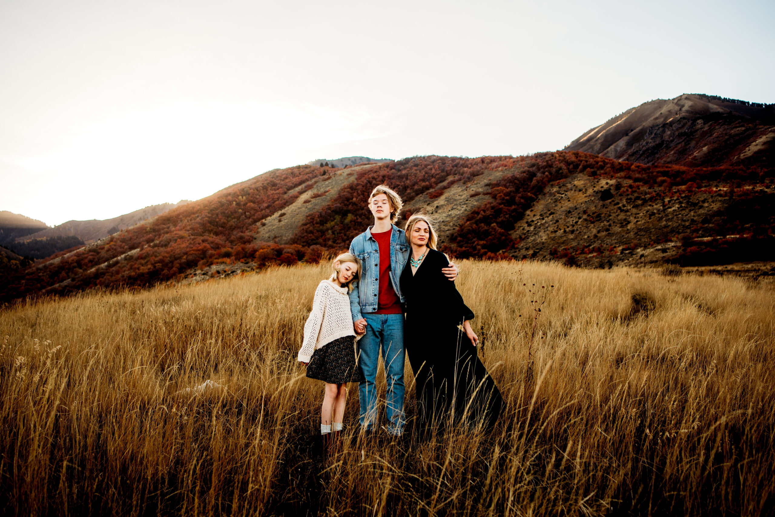 Cream sweater and black dress, dark green dress, jean jacket / Mom embracing son and daughter while looking into distance on hillside / what to wear for family pictures // Photo by Katie Blakeley Creative of Utah. See more at katieblakeley.com/blog